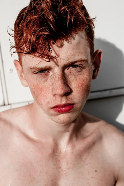 Portrait of attractive stylish young guy model with red hair and freckles standing near white wall , without t-shirt. Fashionable outdoor shot.
