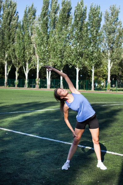 Woman stretching in fitness exercise outside by park. Beautiful fit female fitness girl model on park doing stretch exercising after workout. Healthy lifestyle concept