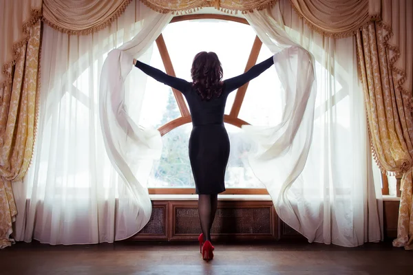 Beautiful slim woman opens the curtains on the window