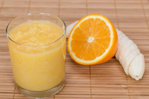 Orange and banana smoothie in glass on orange background