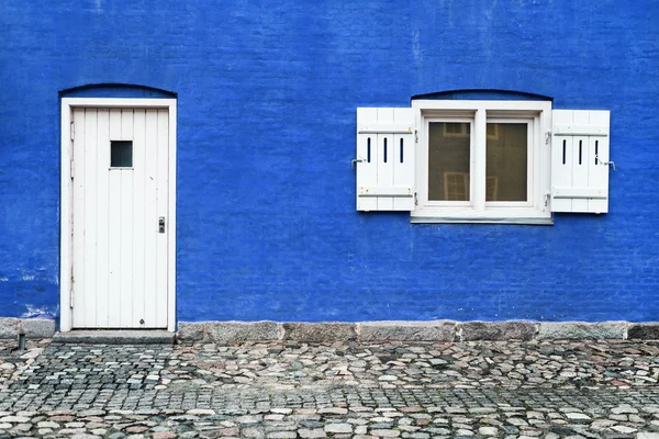 Blue wall with white door and window with opened shutters, facade of the old house