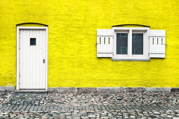 Yellow brick house with white door and window with opened shutters