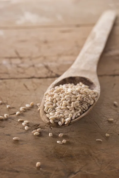 Organic pearl barley on wooden spoon and wooden background, portrait oriented