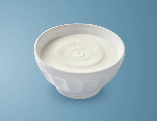 White bowl of milk with drop on blue background