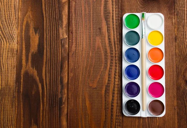 The palette of watercolor paints on a wooden background.