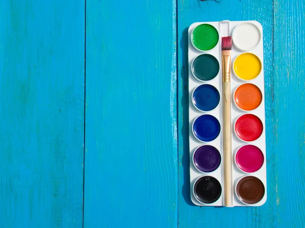 The palette of watercolor paints on a blue wooden background.