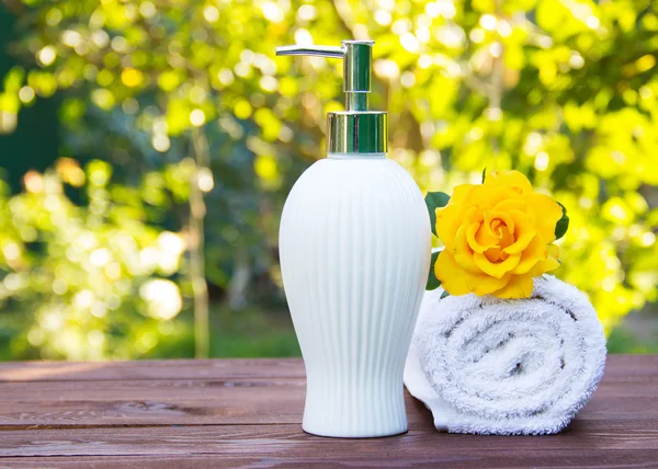 Soap dispenser and white towel. Fragrant yellow rose. Spa concept. Health and beauty. Body Lotion with rose oil. Natural green background. Green blur. Copy space.