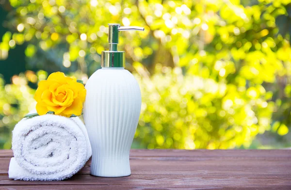Soap dispenser and white towel. Fragrant yellow rose. Spa concept. Health and beauty. Body Lotion. Natural green background. Green blur. Copy space.