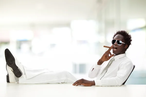 Handsome black businessman with white suit smoking cigar at office