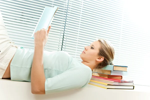 Young beautiful blonde woman read book in a living room with venetian blind window background