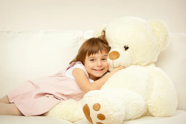 Blonde female child play with her white teddy bear in a bed