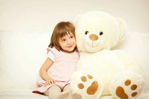 Blonde female child play with her white teddy bear in a bed