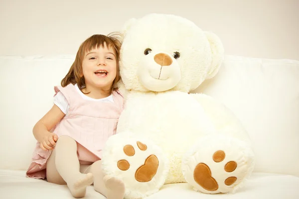 Blonde female child play with her white teddy bear in a bed