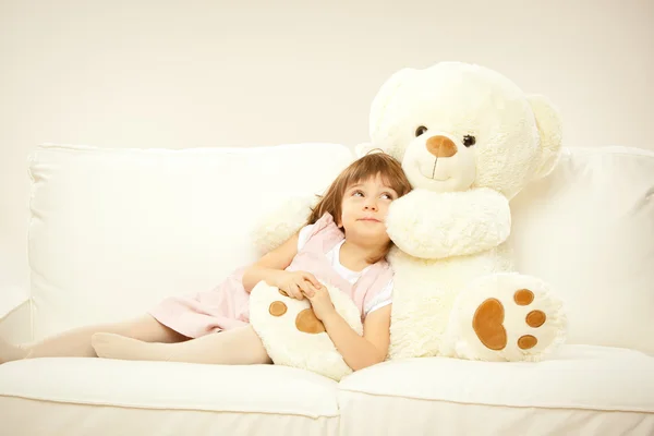 Blonde female child play with her white teddy bear in a bed