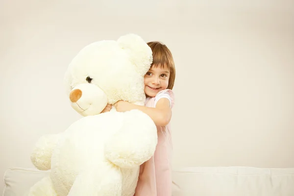 Blonde female child play with her white teddy bear in a bed