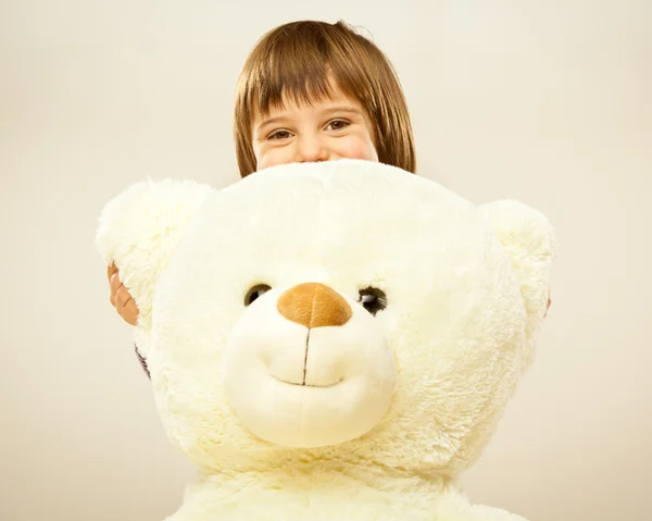 Blonde female child play with her white teddy bear in a bed