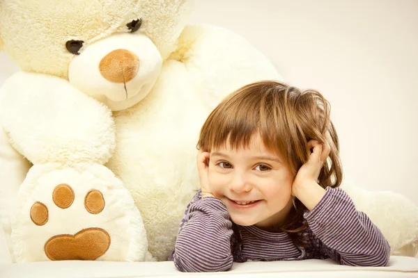 Blonde female child play with her white teddy bear in a bed
