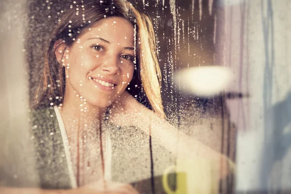 Romantic young woman with cup of tea looks at rain through the window