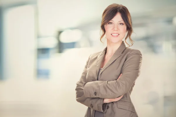 Brunette young businesswoman smiling with arms folded at office