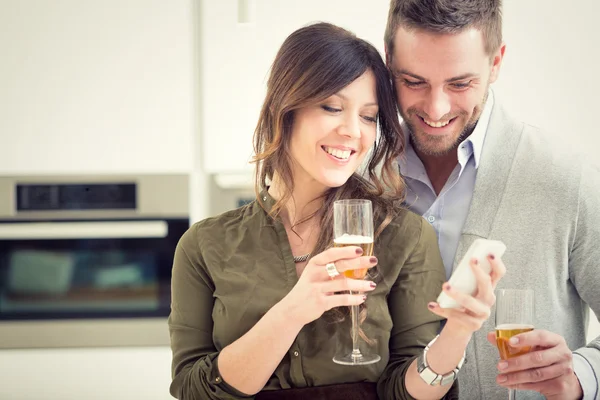 Young casual couple cheers with champagne and phone in the kitchen
