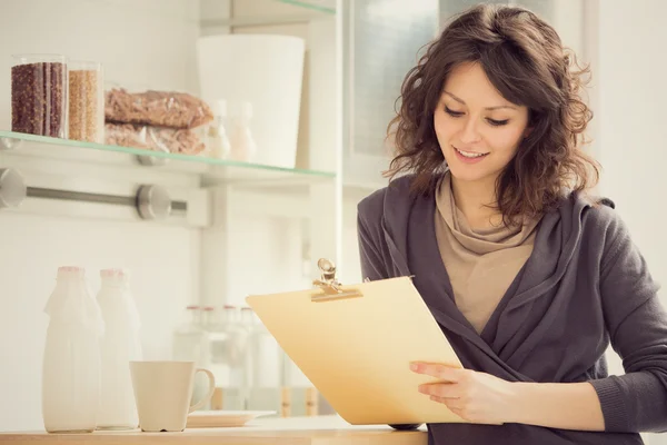 Young smiling brunette woman write in the kitchen