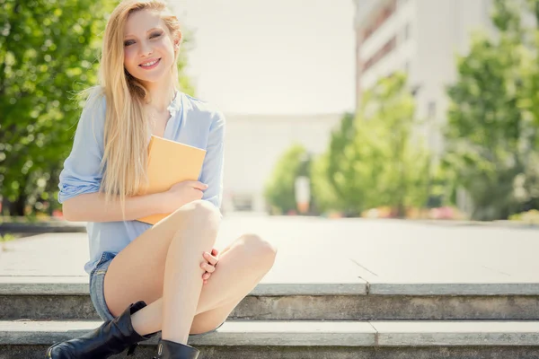 Smiling blonde young woman with book relax in a garden
