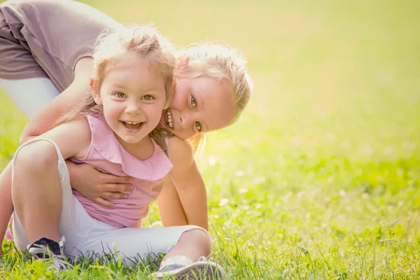 Blonde smiling sister play in a garden