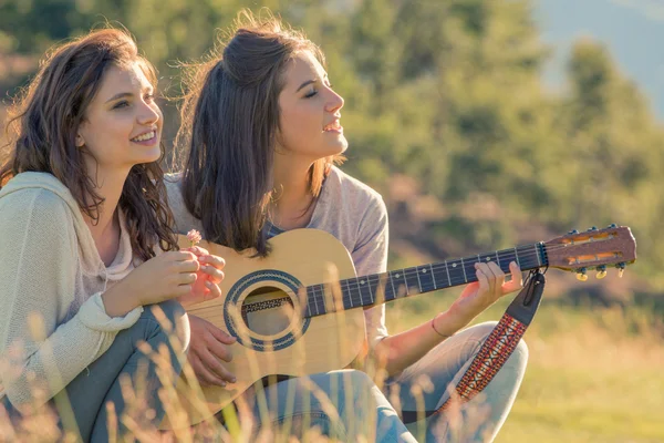 Young woman sing playing guitar with friend on sunset outdoor