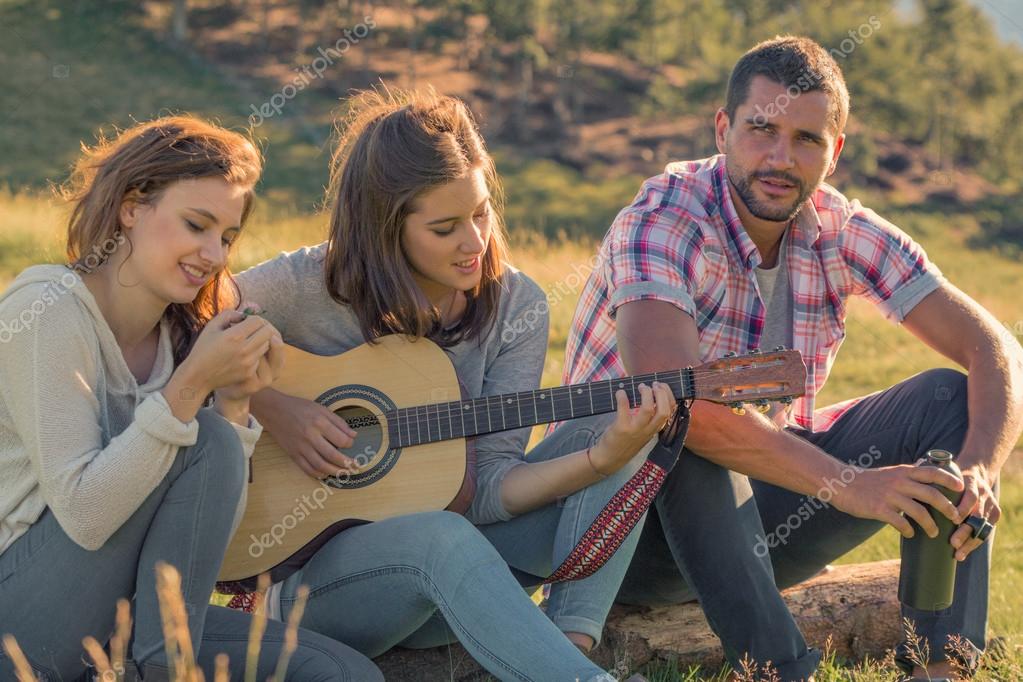 Giovane donna cantare suonare la chitarra con gli amici sul tramonto