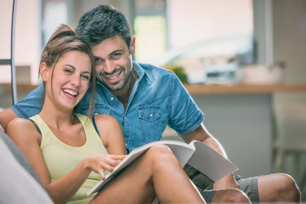Young couple read a magazine seated on couch indoor