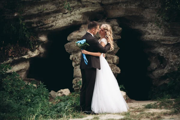 Luxury wedding couple hugging and kissing on the background gorgeous plants and cave near ancient castle