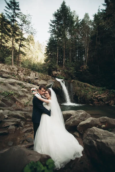 Beautiful wedding couple stay on stone of the river in scenic mountains
