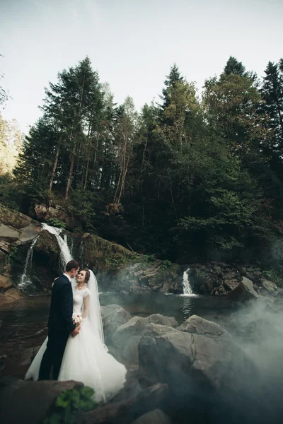 Beautiful wedding couple stay on stone of the river in scenic mountains