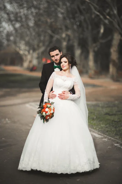 Stylish couple of happy stylish newlyweds walking in the  park on their wedding day with bouquet