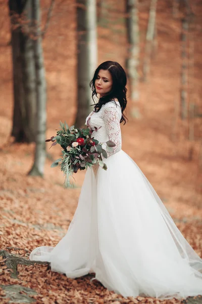 Gorgeous brunette bride in elegant dress holding bouquet  posing near forest and lake