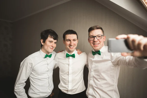 Happy friends helps stylish groom getting ready for his wedding day