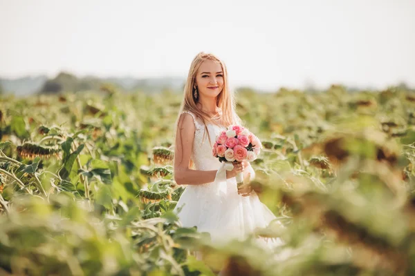 Elegant blonde bride with long hair and a bouquet of sunflowers in the field