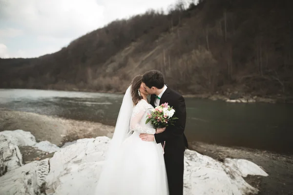 Happy wedding couple, bride and groom posing neat river against backdrop of the mountains