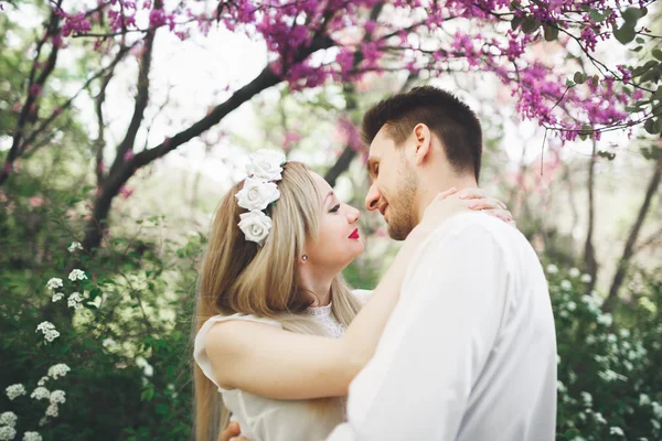 Young beautiful couple kissing and hugging near trees with blossom in summer park