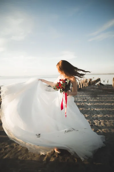 Pretty lady, bride posing in a wedding dress near sea on sunset