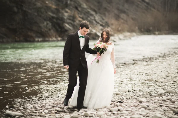 Happy wedding couple, bride and groom posing neat river against backdrop of the mountains