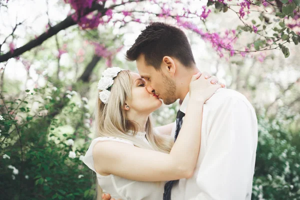 Young beautiful couple kissing and hugging near trees with blossom in summer park