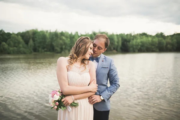 Charming bride, elegant groom on landscapes of mountains and sunset at lake. Gorgeous wedding couple