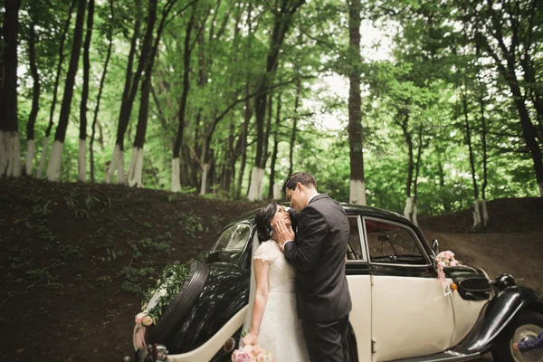 Happy newlywed couple, man and wife kissing near stylish retro car