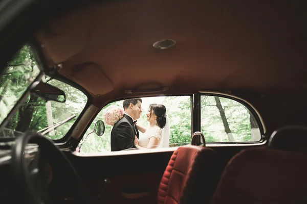 Stylish wedding couple, bride, groom kissing and hugging near retro car in autumn