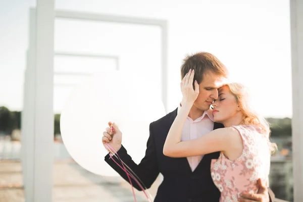 Young couple in love posing on roof with perfect city view holding hands and hugging . Beautiful sunset