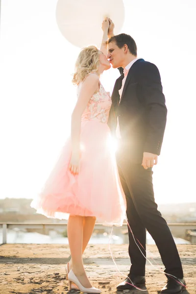 Young couple in love posing on roof with perfect city view holding hands and hugging . Beautiful sunset