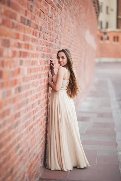 Beautiful sexy girl with long hair and dress perfect shape tanned body possing near wall