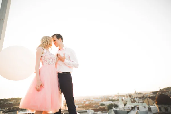 Young couple in love posing on roof with perfect city view holding hands and hugging . Beautiful sunset