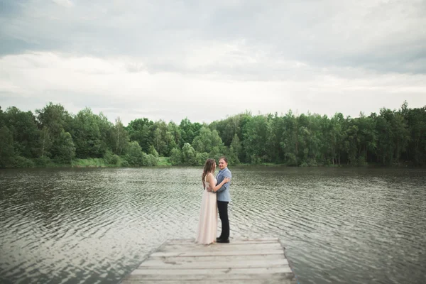 Charming bride, elegant groom on landscapes of mountains and sunset at lake. Gorgeous wedding couple